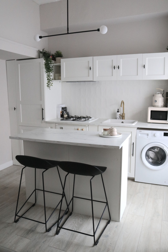 Inspiration för små moderna linjära vitt kök med öppen planlösning, med en undermonterad diskho, skåp i shakerstil, vita skåp, laminatbänkskiva, vitt stänkskydd, stänkskydd i keramik, vita vitvaror, vinylgolv, en köksö och beiget golv