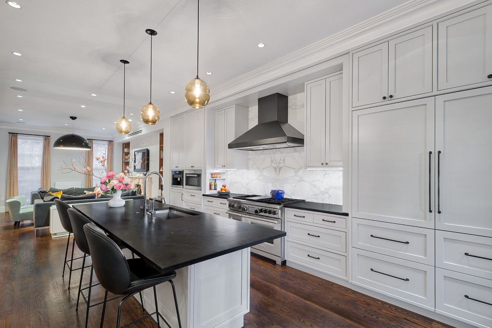 Mid-sized transitional galley open plan kitchen in New York with an undermount sink, white cabinets, soapstone benchtops, white splashback, marble splashback, medium hardwood floors, with island, brown floor and black benchtop.