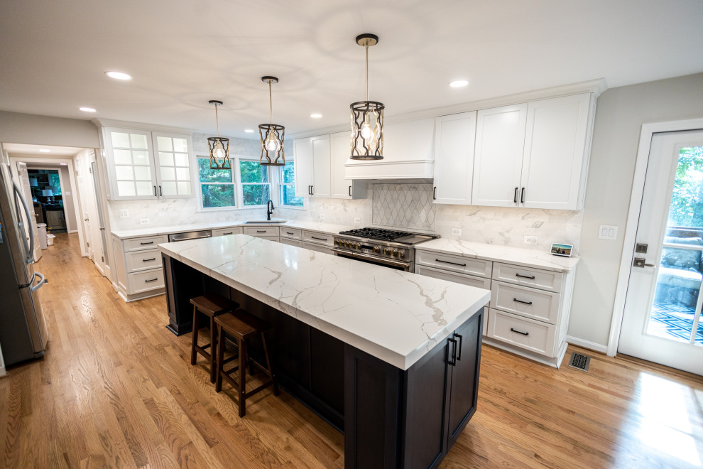 Large transitional l-shaped light wood floor and brown floor eat-in kitchen photo in Baltimore with an undermount sink, shaker cabinets, white cabinets, quartz countertops, white backsplash, marble backsplash, stainless steel appliances, an island and white countertops
