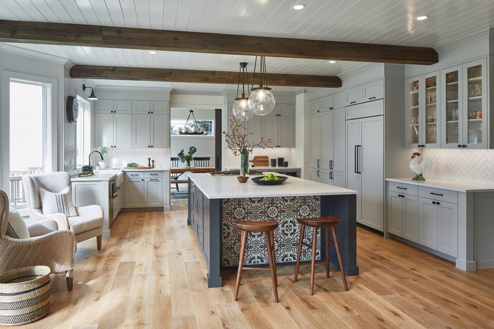 Inspiration for a mid-sized country u-shaped open plan kitchen in Portland with a farmhouse sink, flat-panel cabinets, grey cabinets, quartz benchtops, white splashback, ceramic splashback, panelled appliances, light hardwood floors, with island, white benchtop and exposed beam.