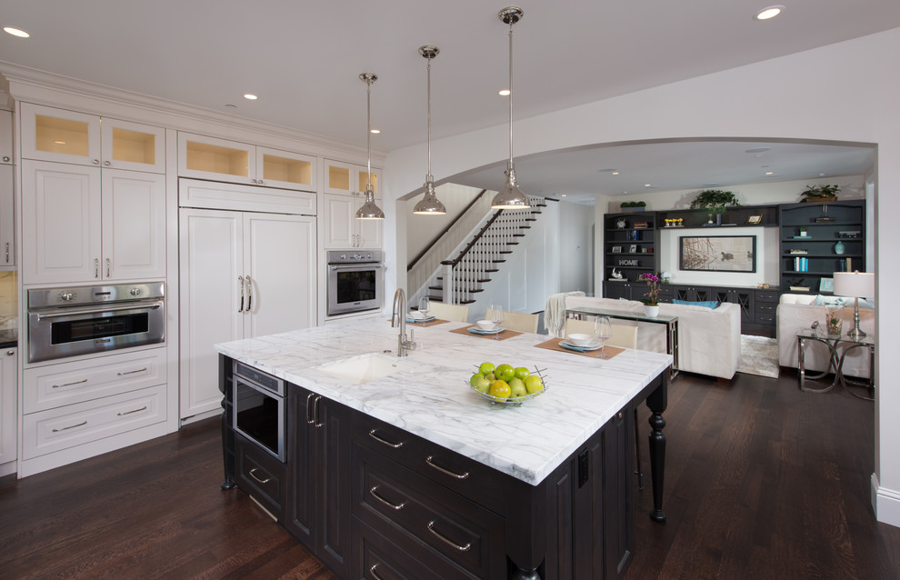 Photo of a mid-sized traditional u-shaped open plan kitchen in San Francisco with an undermount sink, raised-panel cabinets, white cabinets, marble benchtops, white splashback, stone tile splashback, stainless steel appliances, dark hardwood floors and with island.