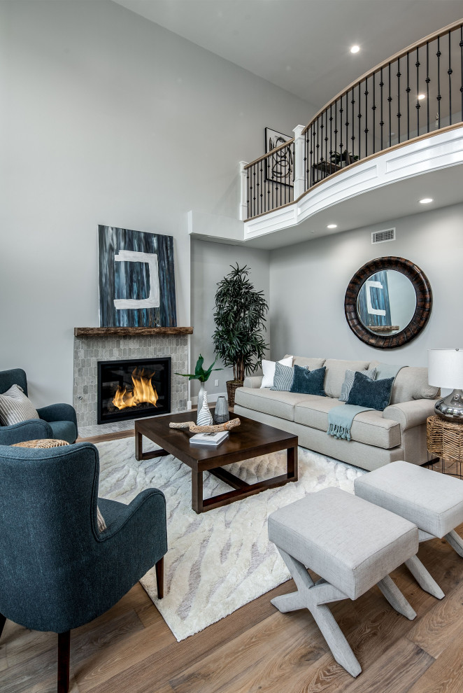 Photo of a large mediterranean family room in San Diego with a home bar, grey walls, light hardwood floors, a standard fireplace, a tile fireplace surround, a wall-mounted tv and beige floor.