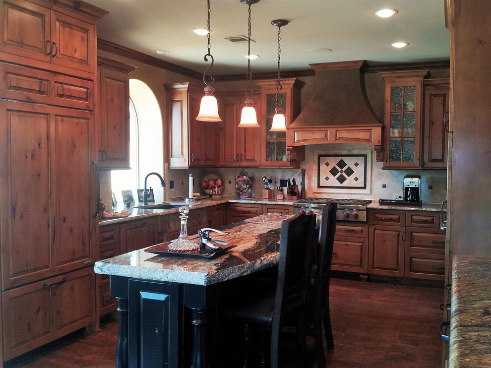 Example of a mid-sized mountain style u-shaped medium tone wood floor eat-in kitchen design in Dallas with an undermount sink, raised-panel cabinets, medium tone wood cabinets, granite countertops, beige backsplash, stone tile backsplash and stainless steel appliances