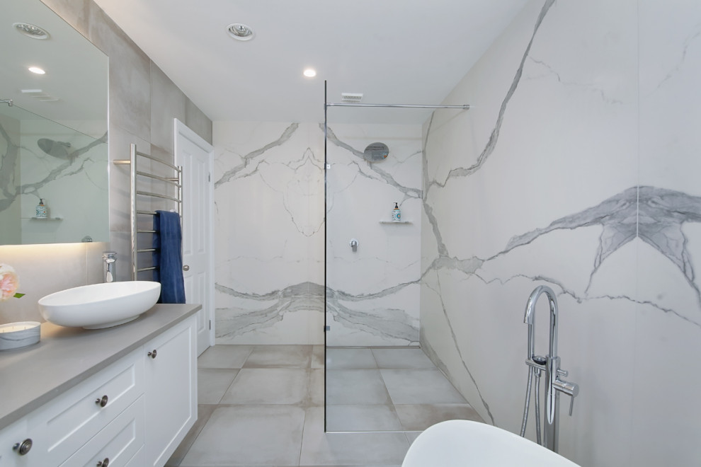 Large modern master wet room bathroom in Sydney with shaker cabinets, white cabinets, a freestanding tub, a one-piece toilet, gray tile, ceramic tile, grey walls, ceramic floors, a pedestal sink, engineered quartz benchtops, grey floor, an open shower and grey benchtops.