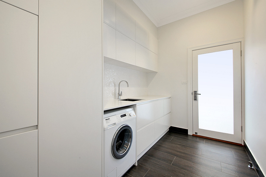 Design ideas for a mid-sized contemporary single-wall dedicated laundry room in Melbourne with an undermount sink, white cabinets, quartz benchtops, white walls, porcelain floors, flat-panel cabinets and an integrated washer and dryer.