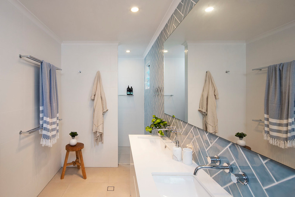 This is an example of a mid-sized beach style master bathroom in Sunshine Coast with white cabinets, a corner shower, a one-piece toilet, blue tile, ceramic tile, multi-coloured walls, ceramic floors, an undermount sink, engineered quartz benchtops, beige floor, an open shower and white benchtops.
