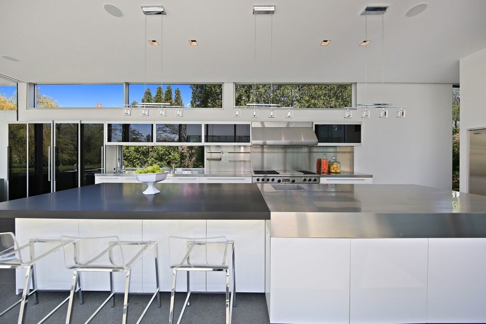 Photo of a large contemporary l-shaped eat-in kitchen in Chicago with stainless steel benchtops, metallic splashback, stainless steel appliances, with island, grey floor, concrete floors and grey benchtop.