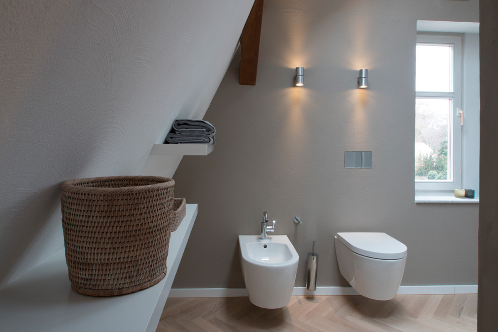 Badezimmer With freistehender Badewanne, bodengleicher Dusche, Wandtoilette, grauer Wandfarbe, braunem Holzboden and integriertem Waschbecken in Berlin