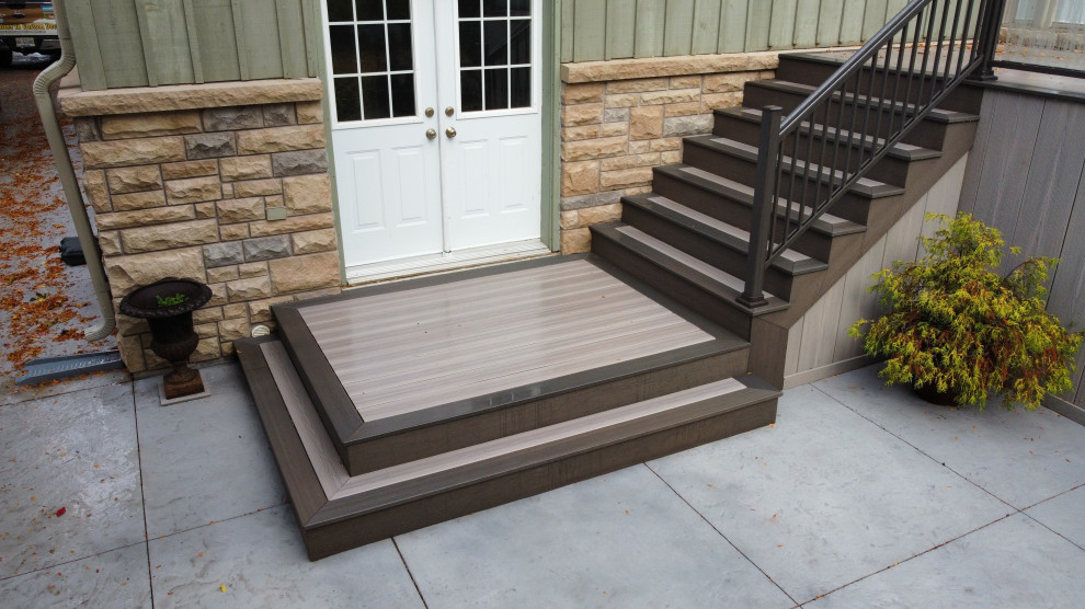 Inspiration for a large transitional backyard and ground level deck with with skirting, an awning and glass railing.