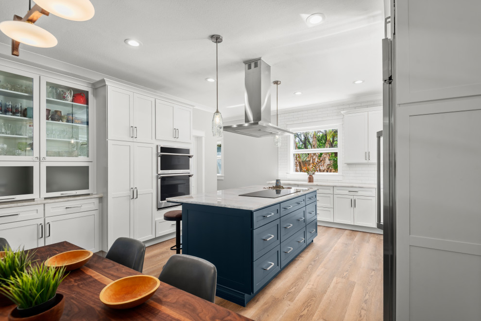 Inspiration for a mid-sized contemporary l-shaped eat-in kitchen in Tampa with an undermount sink, shaker cabinets, blue cabinets, quartz benchtops, white splashback, ceramic splashback, stainless steel appliances, vinyl floors, with island, brown floor and beige benchtop.