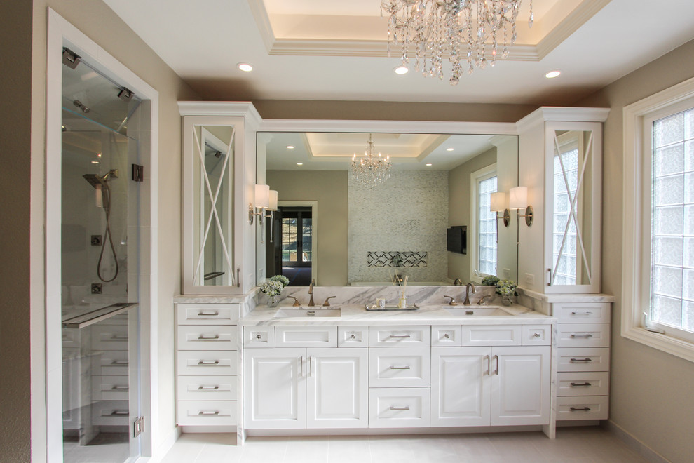 Photo of a large traditional master bathroom in San Francisco with an undermount sink, shaker cabinets, white cabinets, marble benchtops, a drop-in tub, a double shower, a one-piece toilet, white tile, stone tile, beige walls and porcelain floors.