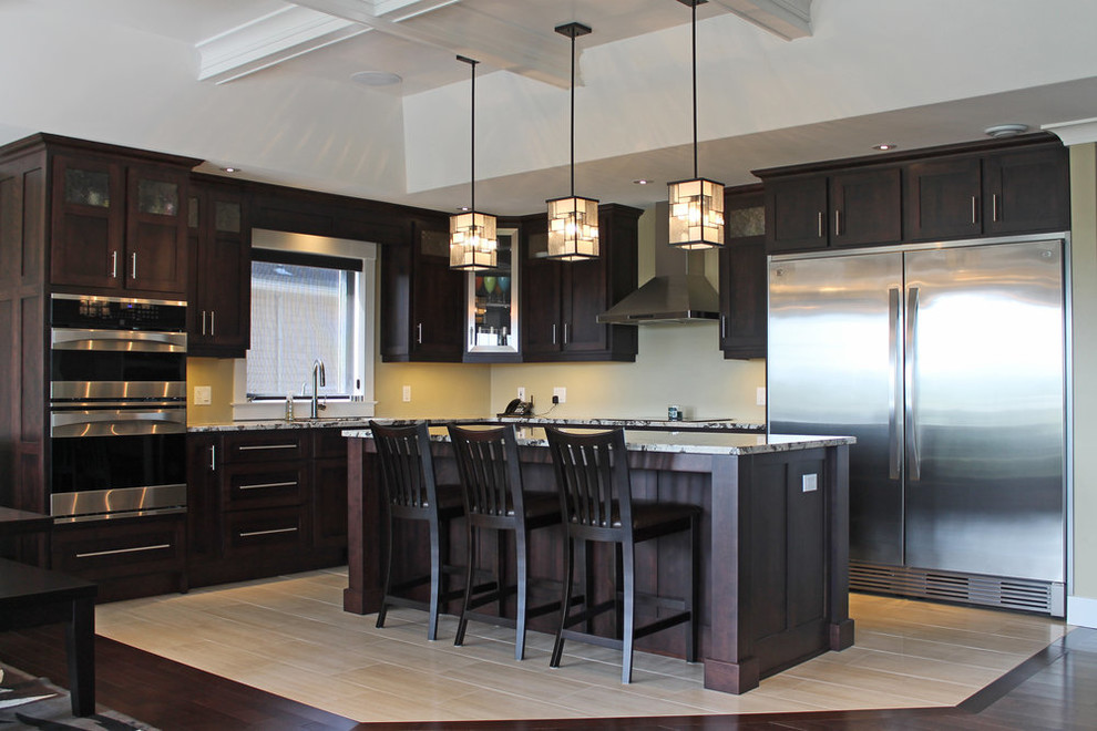 Mid-sized transitional l-shaped light wood floor and beige floor open concept kitchen photo with recessed-panel cabinets, dark wood cabinets, granite countertops, stainless steel appliances, an island and gray countertops