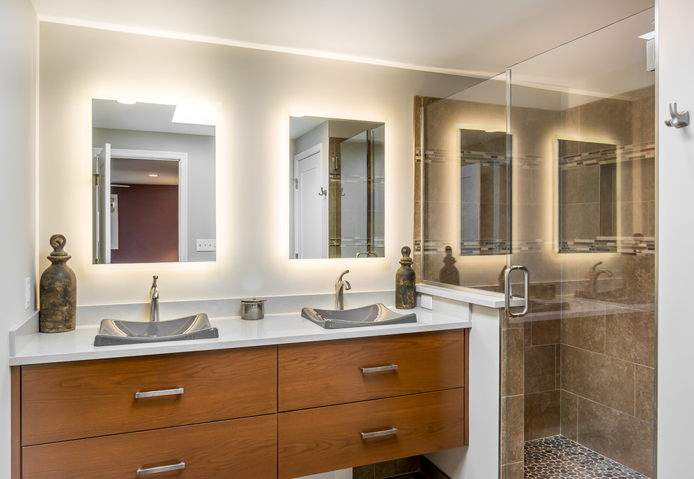 Photo of a mid-sized contemporary master bathroom in Detroit with flat-panel cabinets, medium wood cabinets, an open shower, beige tile, porcelain tile, grey walls, a drop-in sink, engineered quartz benchtops, pebble tile floors, multi-coloured floor, a hinged shower door and grey benchtops.