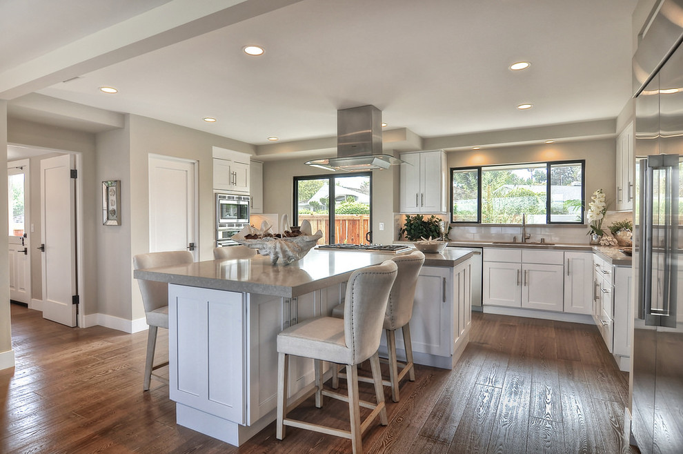 Example of a mid-sized transitional light wood floor eat-in kitchen design in Orange County with an undermount sink, shaker cabinets, white cabinets, solid surface countertops, white backsplash, ceramic backsplash and stainless steel appliances