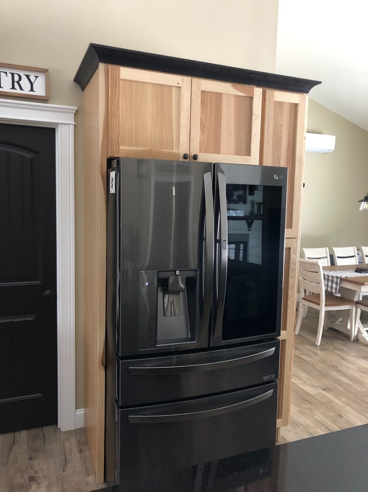 This is an example of a country l-shaped open plan kitchen in Other with a farmhouse sink, flat-panel cabinets, light wood cabinets, granite benchtops, with island and black benchtop.