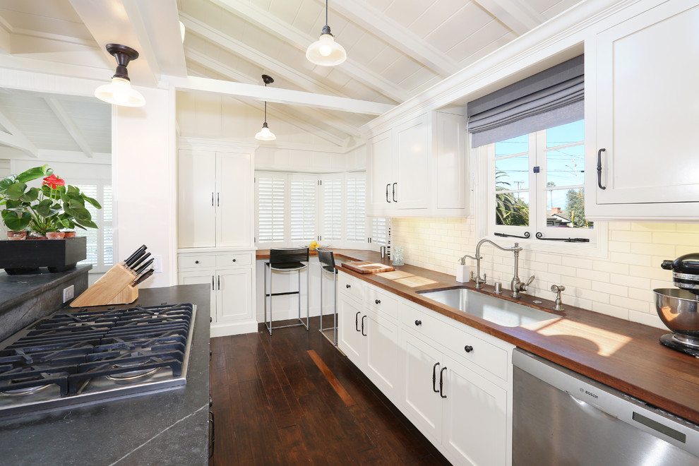 This is an example of a traditional u-shaped kitchen in Orange County with an undermount sink, flat-panel cabinets, white cabinets, wood benchtops, white splashback, white appliances and dark hardwood floors.