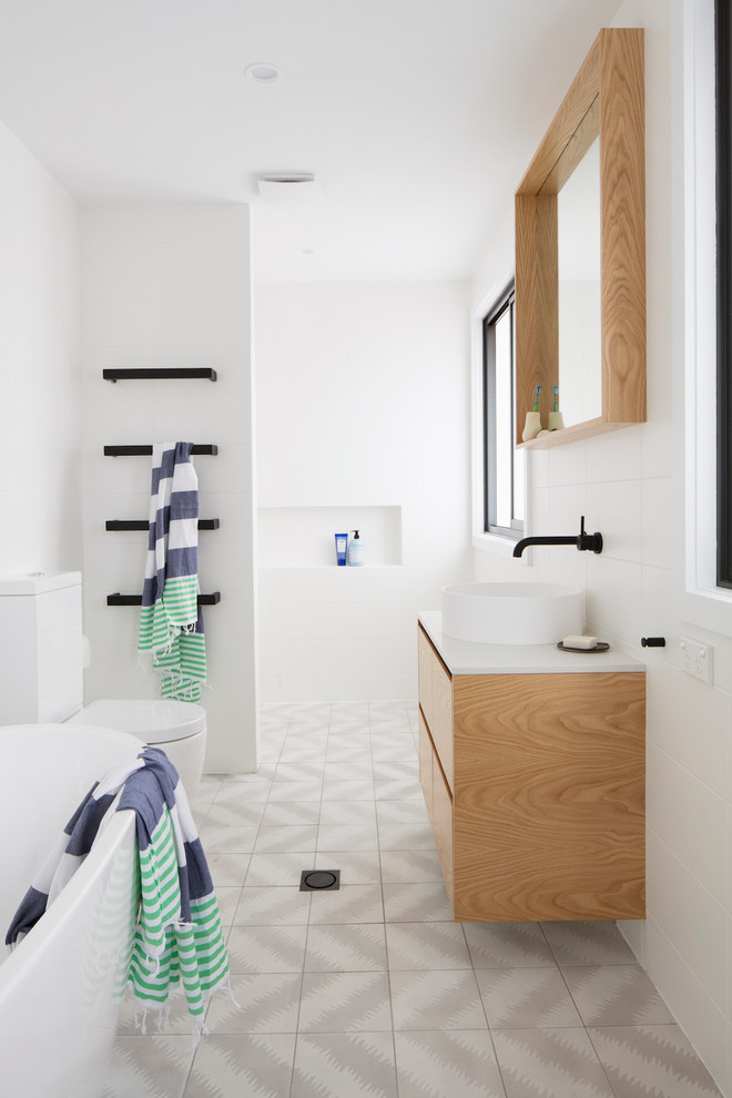 This is an example of a contemporary master bathroom in Brisbane with flat-panel cabinets, light wood cabinets, a freestanding tub, a curbless shower, a two-piece toilet, gray tile, white walls, cement tiles, a vessel sink and an open shower.