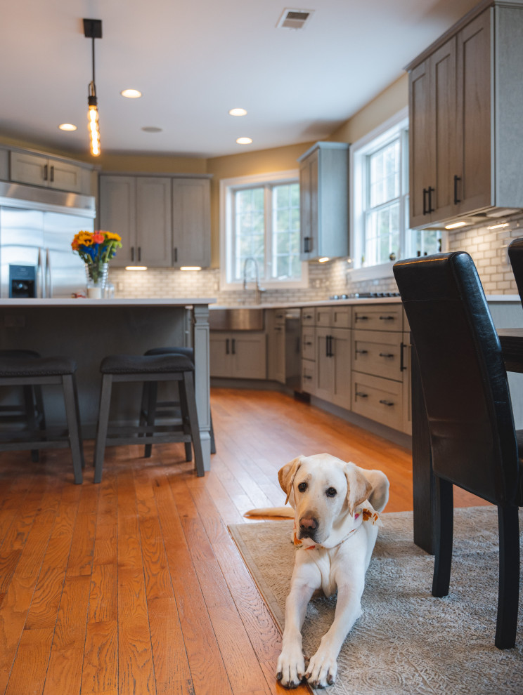 Inspiration for a large transitional u-shaped medium tone wood floor and brown floor eat-in kitchen remodel with a farmhouse sink, shaker cabinets, gray cabinets, quartz countertops, gray backsplash, glass tile backsplash, stainless steel appliances, an island and white countertops