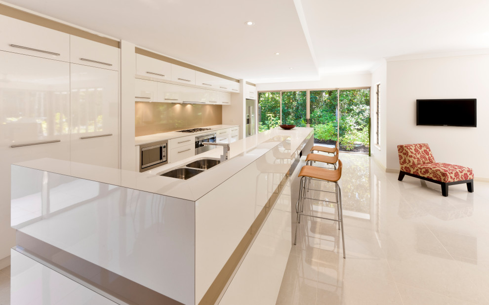 Inspiration for a mid-sized tropical galley kitchen in Cairns with an undermount sink, white cabinets, solid surface benchtops, metallic splashback, glass tile splashback, stainless steel appliances, slate floors, with island and beige floor.