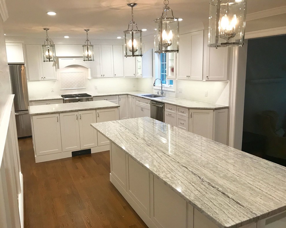 Inspiration for a large transitional l-shaped dark wood floor and brown floor enclosed kitchen remodel with an undermount sink, shaker cabinets, white cabinets, marble countertops, white backsplash, ceramic backsplash, stainless steel appliances and two islands
