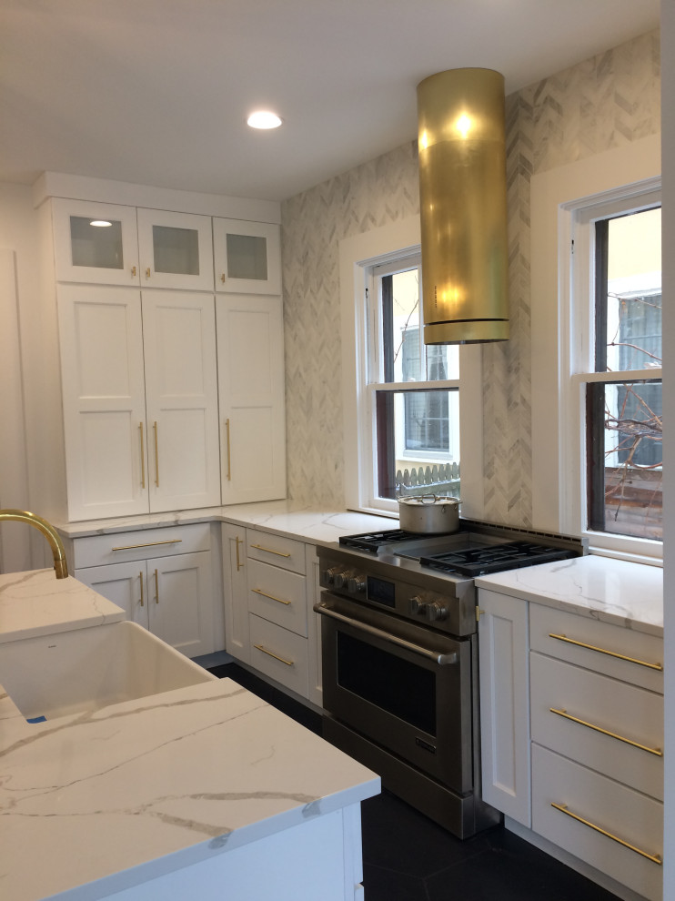 This is an example of a mid-sized transitional l-shaped eat-in kitchen in New York with a farmhouse sink, shaker cabinets, white cabinets, quartzite benchtops, grey splashback, stone tile splashback, ceramic floors, with island, black floor and white benchtop.