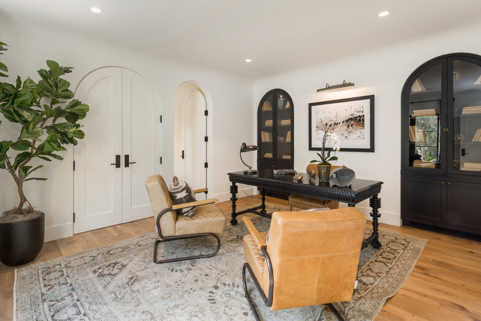 This is an example of a mediterranean study room in Los Angeles with white walls, light hardwood floors, no fireplace and a freestanding desk.