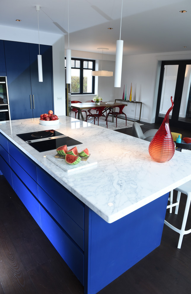 This is an example of a mid-sized modern l-shaped kitchen in Dublin with an integrated sink, flat-panel cabinets, blue cabinets, marble benchtops, white splashback, engineered quartz splashback, black appliances, dark hardwood floors, with island, black floor and white benchtop.