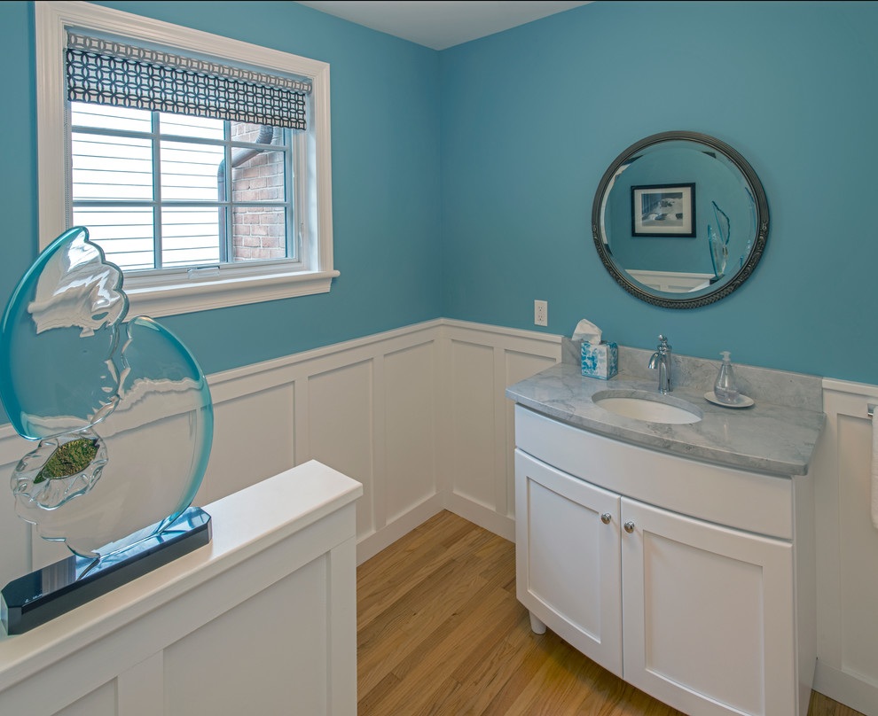 This is an example of a traditional powder room in Philadelphia with recessed-panel cabinets, white cabinets, blue walls, light hardwood floors, an undermount sink and marble benchtops.