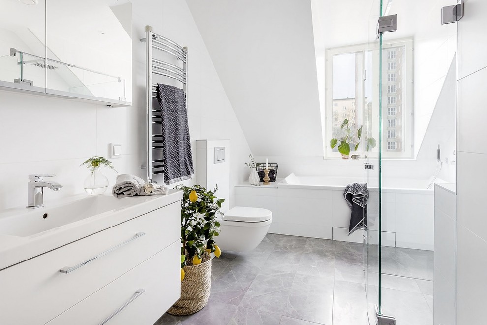 Inspiration for a mid-sized scandinavian bathroom in Stockholm with flat-panel cabinets, white cabinets, a corner shower, white walls, a wall-mount toilet, white tile, limestone floors, an integrated sink and a drop-in tub.