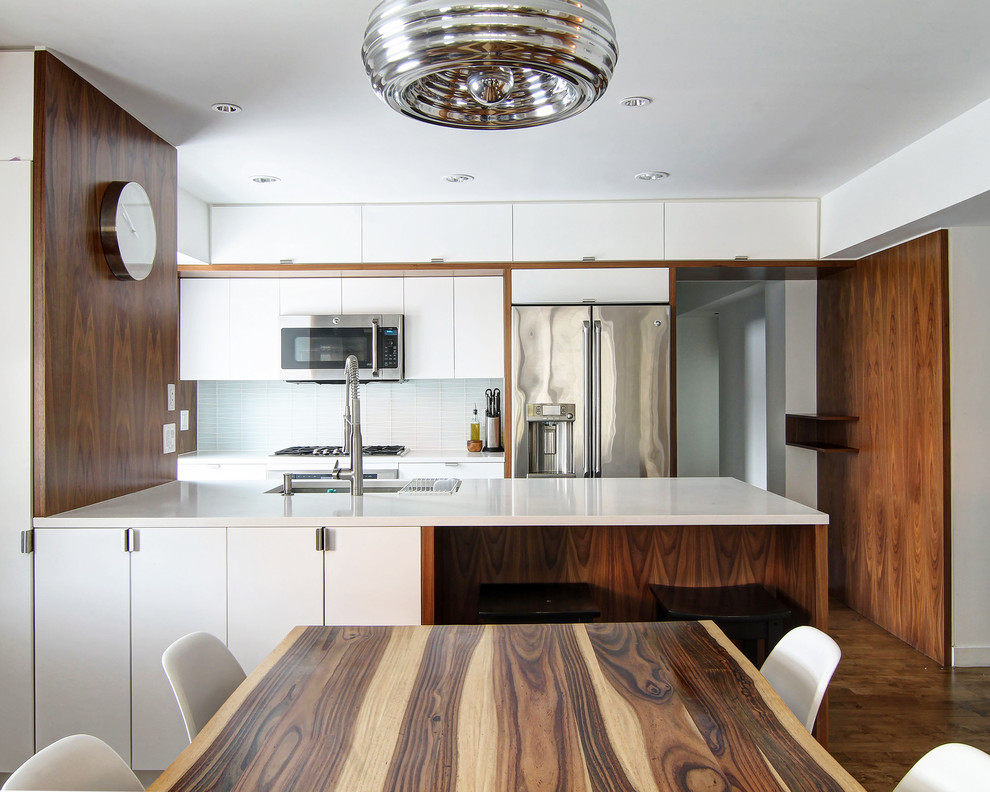 Design ideas for a mid-sized modern galley open plan kitchen in New York with an undermount sink, flat-panel cabinets, white cabinets, quartz benchtops, blue splashback, glass tile splashback, stainless steel appliances, porcelain floors, a peninsula and brown floor.