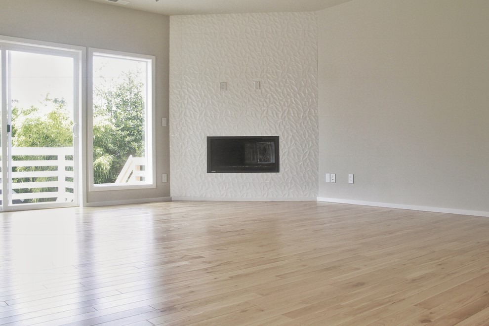 This is an example of a mid-sized contemporary open concept living room in Portland with beige walls, light hardwood floors, a corner fireplace, a plaster fireplace surround and no tv.