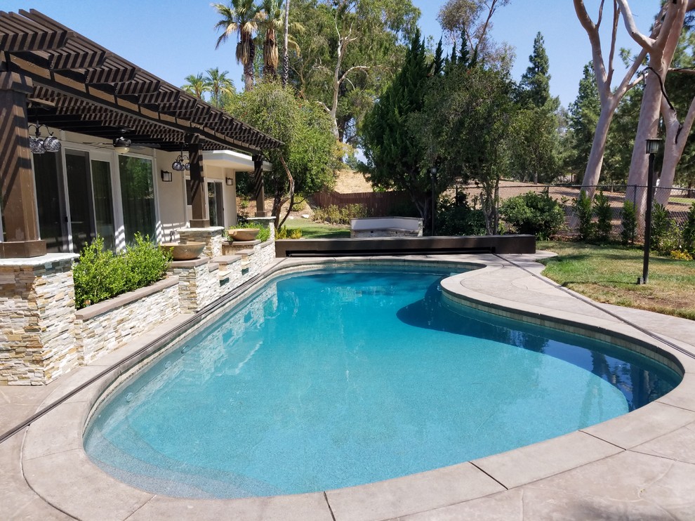 Inspiration for a large modern backyard custom-shaped aboveground pool in Los Angeles with a water feature and stamped concrete.