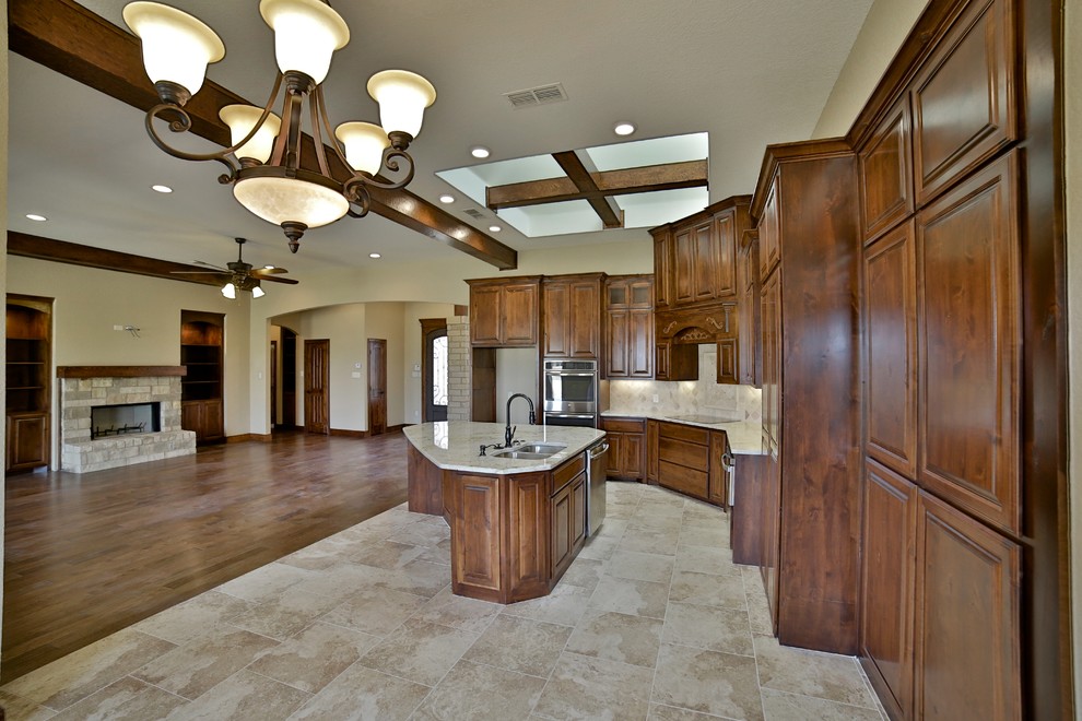 Eat-in kitchen - mid-sized rustic l-shaped porcelain tile eat-in kitchen idea in Dallas with an undermount sink, raised-panel cabinets, medium tone wood cabinets, granite countertops, beige backsplash, stone tile backsplash, stainless steel appliances and an island