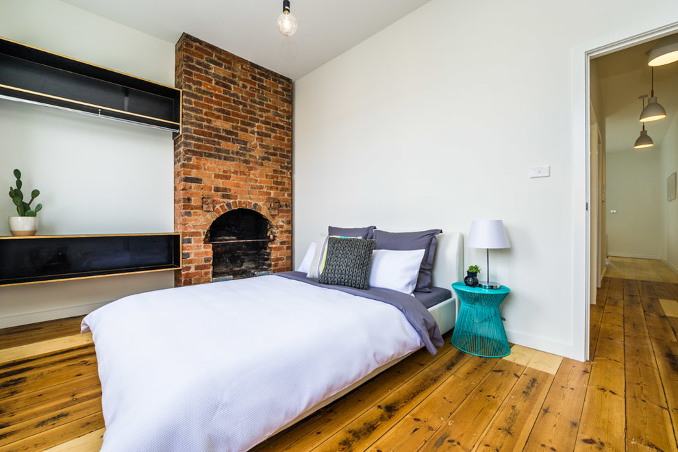 This is an example of a small industrial master bedroom in Hobart with white walls, medium hardwood floors, a standard fireplace and a brick fireplace surround.