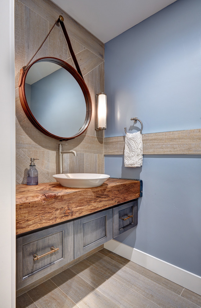 Design ideas for a small eclectic powder room in Sacramento with a vessel sink, recessed-panel cabinets, grey cabinets, wood benchtops, gray tile, porcelain tile, blue walls, porcelain floors and brown benchtops.