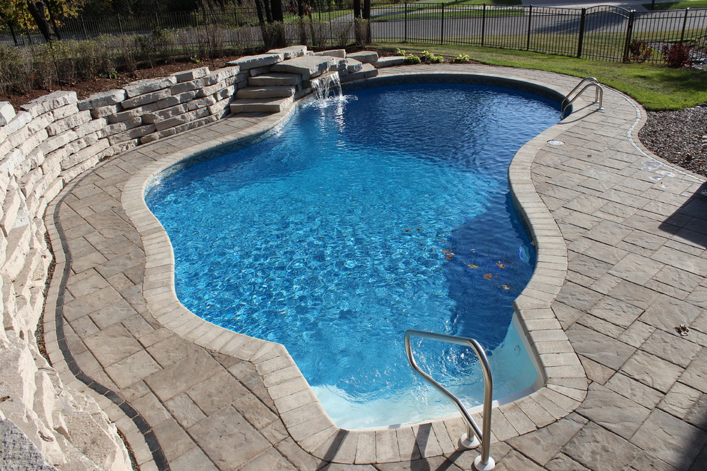 Photo of a large transitional backyard custom-shaped natural pool in Chicago with a water feature and brick pavers.