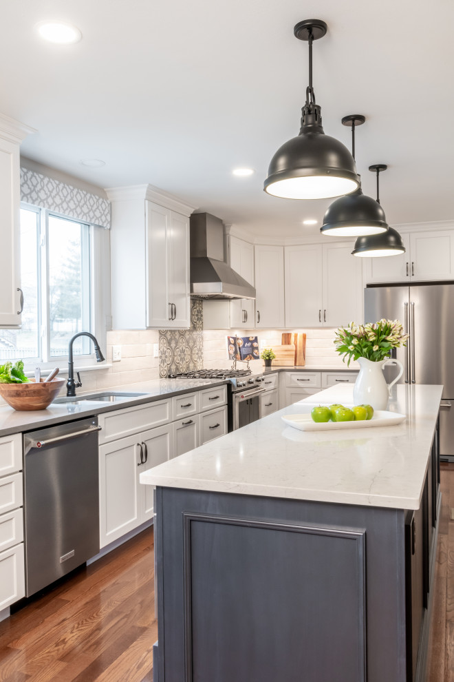 Example of a large transitional l-shaped medium tone wood floor and brown floor eat-in kitchen design in St Louis with an undermount sink, shaker cabinets, quartz countertops, porcelain backsplash, stainless steel appliances, an island, white cabinets, white backsplash and white countertops