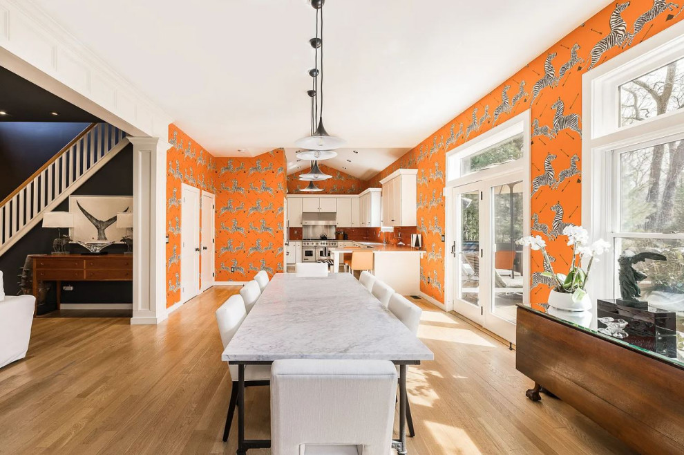 Photo of a medium sized eclectic dining room in New York with orange walls, light hardwood flooring, beige floors, a vaulted ceiling and wallpapered walls.