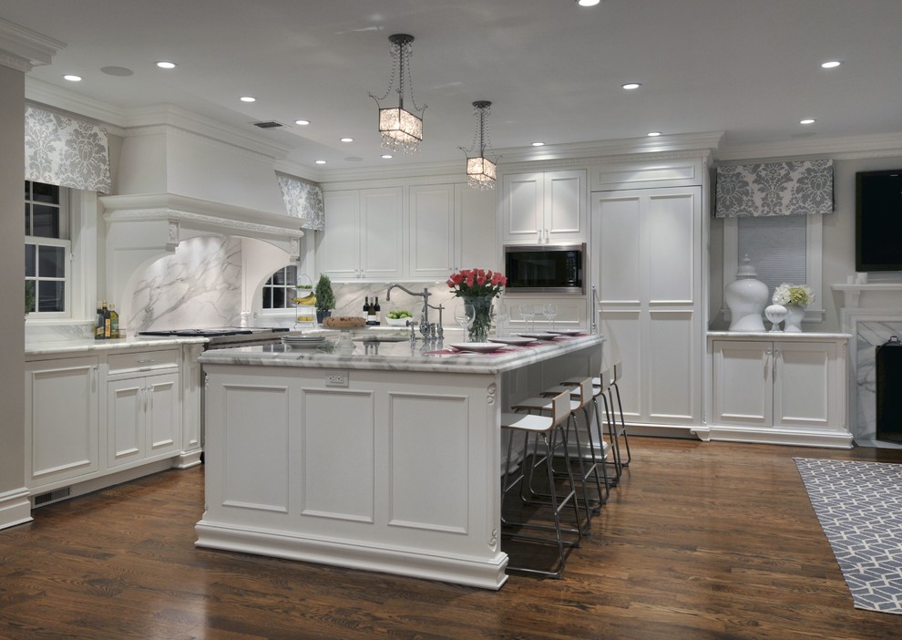 Inspiration for a large transitional l-shaped eat-in kitchen in New York with an integrated sink, recessed-panel cabinets, white cabinets, marble benchtops, white splashback, stone slab splashback, medium hardwood floors and with island.