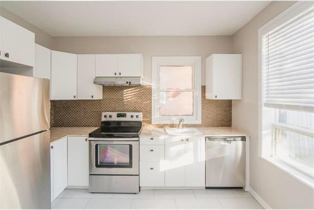 Example of a mid-sized transitional l-shaped porcelain tile and gray floor eat-in kitchen design in Toronto with a drop-in sink, flat-panel cabinets, white cabinets, marble countertops, metallic backsplash, mosaic tile backsplash, stainless steel appliances, no island and beige countertops