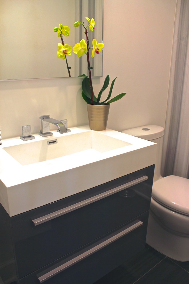 This is an example of a small modern powder room in New York with an integrated sink, flat-panel cabinets, grey cabinets, solid surface benchtops, a one-piece toilet, gray tile and white walls.
