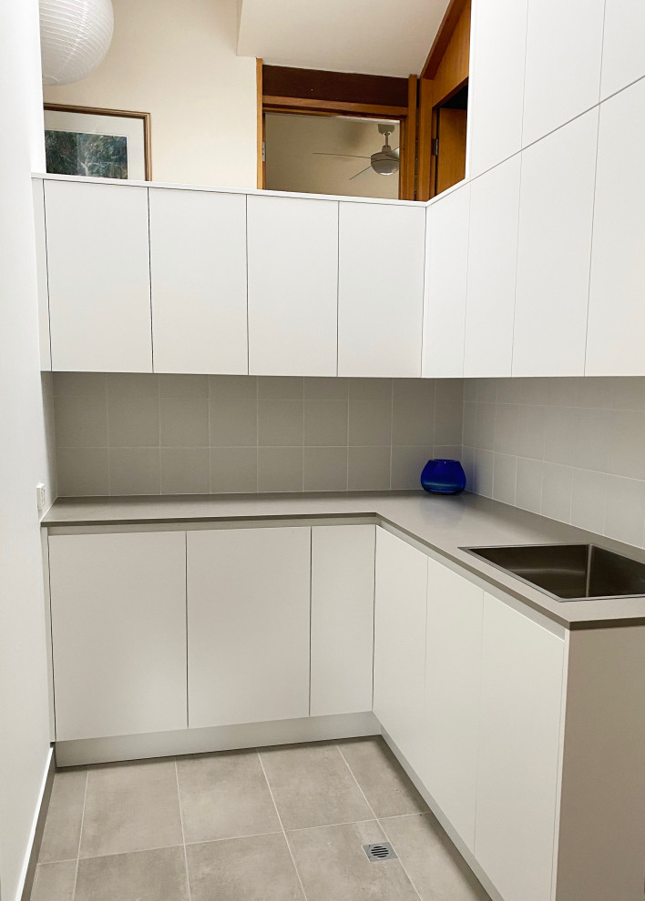 Design ideas for a large modern l-shaped dedicated laundry room in Sydney with a drop-in sink, flat-panel cabinets, white cabinets, quartz benchtops, grey splashback, ceramic splashback, grey walls, porcelain floors, a stacked washer and dryer, grey floor, grey benchtop, vaulted and brick walls.