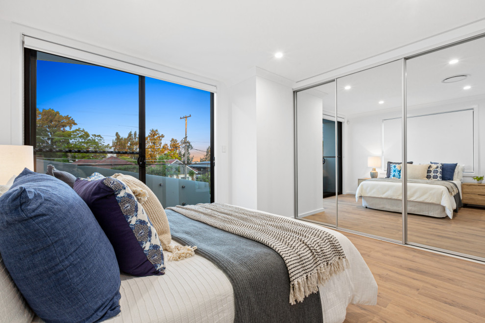 Photo of a large contemporary master bedroom in Sydney with white walls, laminate floors and brown floor.