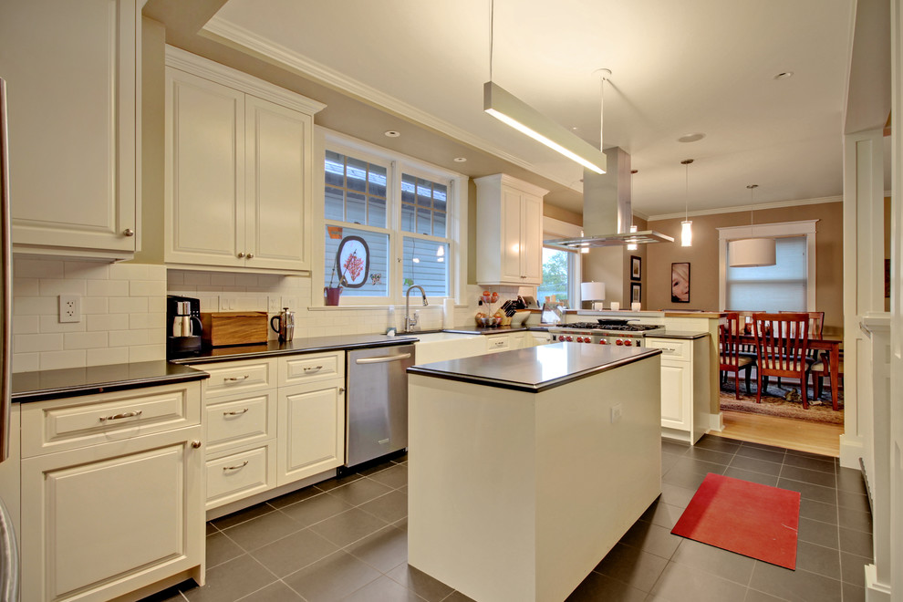 Photo of a mid-sized arts and crafts u-shaped eat-in kitchen in Seattle with a farmhouse sink, raised-panel cabinets, white cabinets, white splashback, subway tile splashback, stainless steel appliances, porcelain floors and with island.