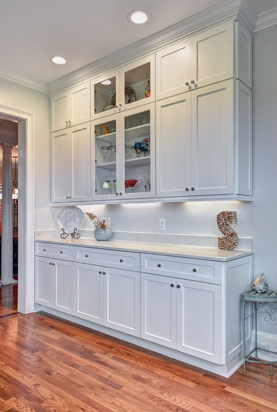 Inspiration for a mid-sized beach style l-shaped eat-in kitchen in Charleston with shaker cabinets, white cabinets, quartz benchtops, medium hardwood floors, a farmhouse sink, grey splashback, glass tile splashback, white appliances, no island, brown floor and white benchtop.