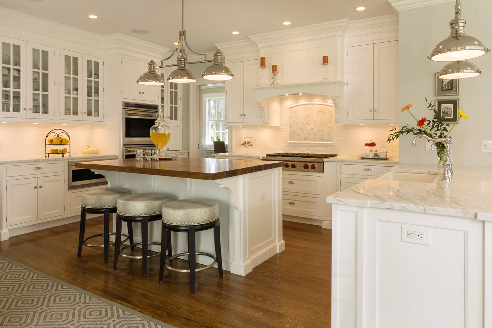 Huge transitional medium tone wood floor kitchen photo in New York with glass-front cabinets, marble countertops, white backsplash, porcelain backsplash, stainless steel appliances and two islands