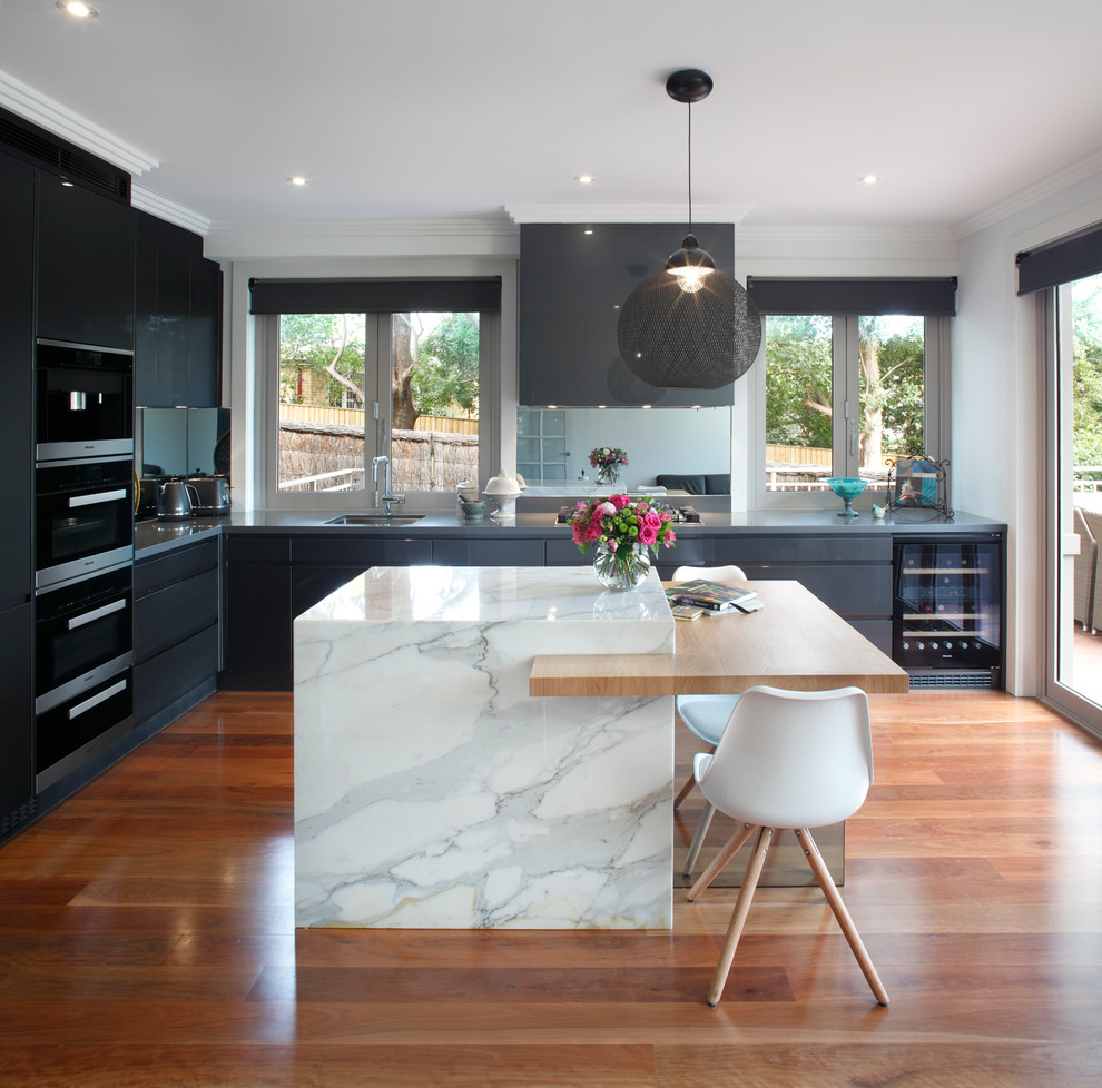 This is an example of a mid-sized contemporary l-shaped eat-in kitchen in Sydney with an undermount sink, grey cabinets, marble benchtops, mirror splashback, black appliances, flat-panel cabinets, medium hardwood floors and multiple islands.