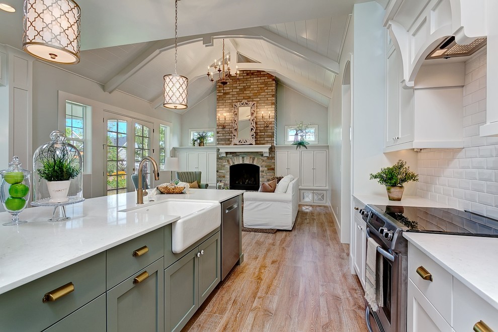 Design ideas for a large beach style galley open plan kitchen in Boise with a farmhouse sink, shaker cabinets, white cabinets, quartz benchtops, white splashback, porcelain splashback, stainless steel appliances, medium hardwood floors and a peninsula.