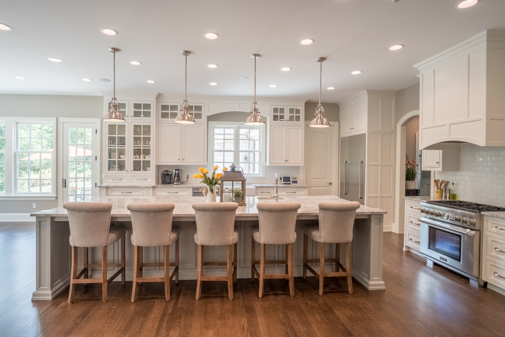 Example of a large transitional l-shaped medium tone wood floor eat-in kitchen design with a farmhouse sink, shaker cabinets, white cabinets, granite countertops, white backsplash, subway tile backsplash, stainless steel appliances and an island