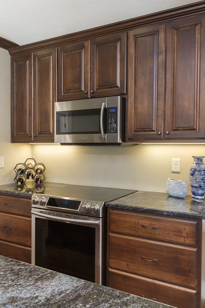 This is an example of a mid-sized traditional l-shaped eat-in kitchen in Tampa with raised-panel cabinets, brown cabinets, granite benchtops, stainless steel appliances, with island and black benchtop.